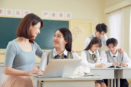 女教师使用笔记本电脑给学生辅导初中生高清图片素材