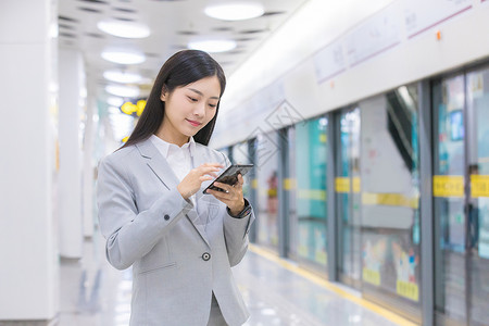 女性白领在地铁旁刷手机高清图片
