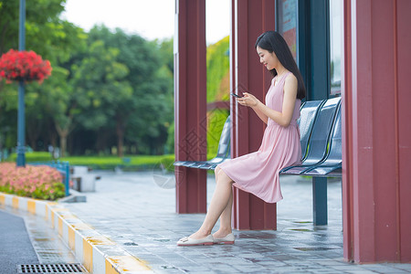 坐在公交站台玩手机的女性背景图片