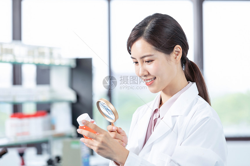 女性医疗科研人员拿放大镜观察新研制药品图片