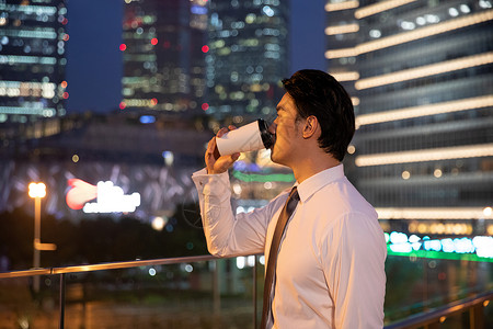 夜晚天桥上的都市商务男性喝咖啡图片