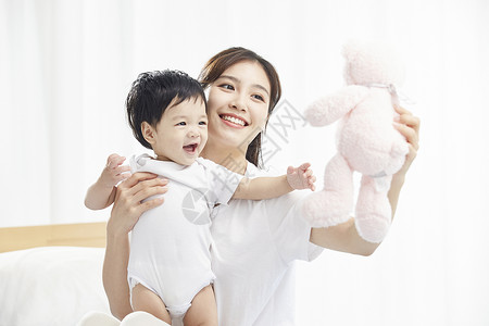 微笑温馨年轻妈妈用毛绒玩具逗宝宝开心背景