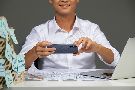使用手机拍摄设计图纸的商务男性图片