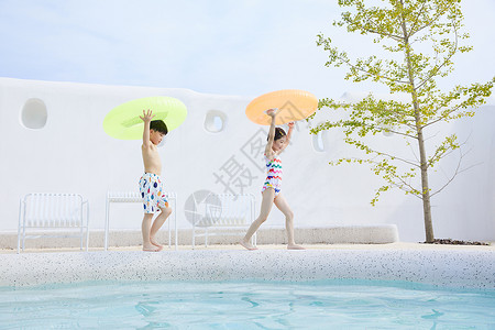 小男孩和小女孩拿着泳圈在泳池边行走高清图片
