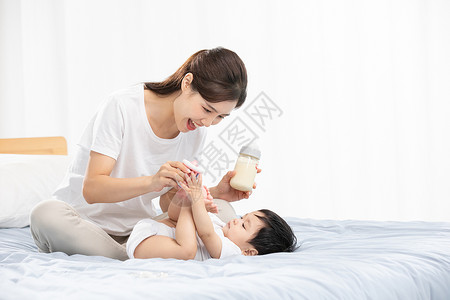 坐着喝奶的婴儿年轻妈妈用奶瓶辅助宝宝喝奶背景