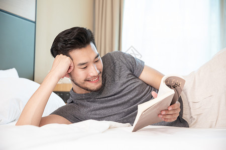 男性出差躺在酒店床上看书图片