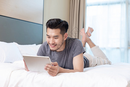 商务男性趴在酒店床上玩平板电脑图片