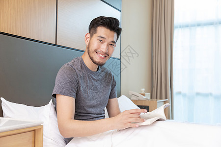 男性出差躺在酒店床上看书背景图片
