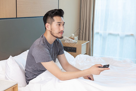 男性躺在酒店床上看电视图片