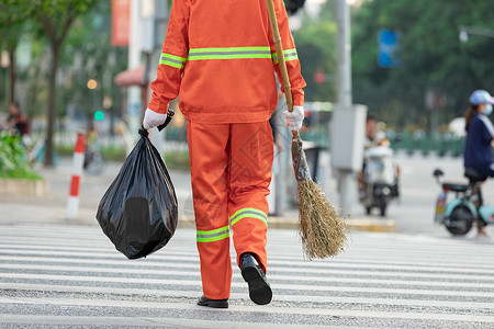 垃圾清理拎着垃圾袋与扫帚的环卫工人过马路背景