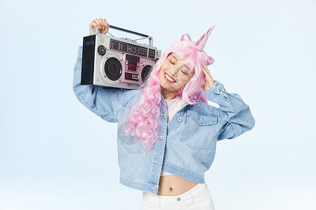 录音机放在肩膀上享受音乐的时尚粉色长发美女高清图片