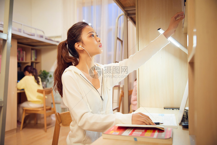 夜晚女学生戴着耳机在宿舍认真复习功课图片