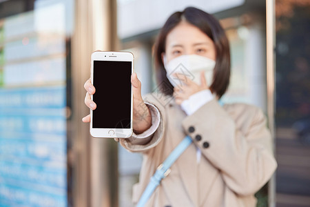 手机保护壳戴口罩在公交站台等待公交车的女性展示手机背景