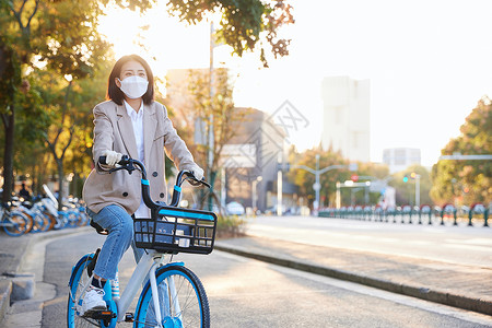 除菌液佩戴口罩与手套的都市女性骑共享单车背景