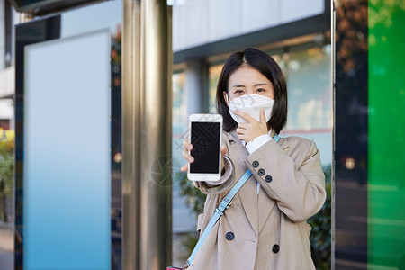 手机保护壳戴口罩在公交站台等待公交车的女性展示手机背景