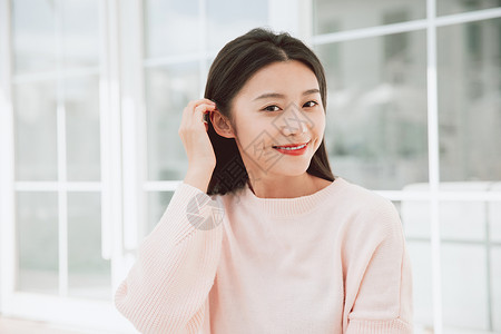 穿着粉色毛衣的美女对着镜头微笑撩头发背景图片