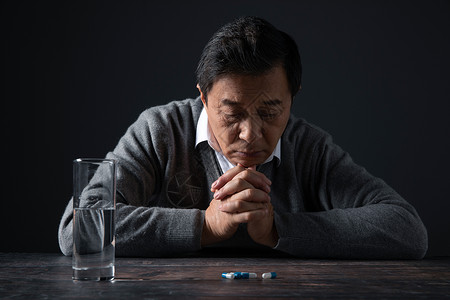 老人面对桌子上的药丸双手合十背景图片