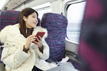 坐在火车上的女性戴着耳机听音乐高清图片