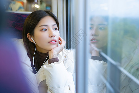 坐在火车上戴着耳机看窗外风景的女性图片