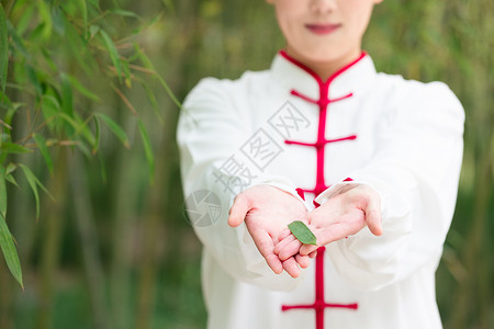 穿着太极服的女性手里捧着一片竹叶背景图片