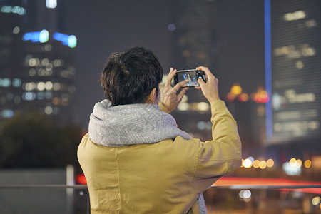 夜晚男青年用手机拍摄城市夜景背景图片