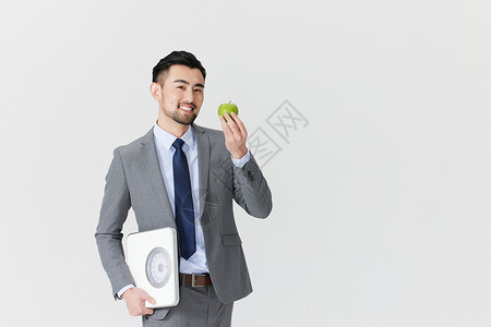 手拿体重秤和青苹果的职场男性图片