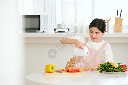 蔬菜机的年轻女性厨房使用打蛋机打蛋背景