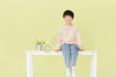 地球上植物坐在桌子上微笑的小男孩背景