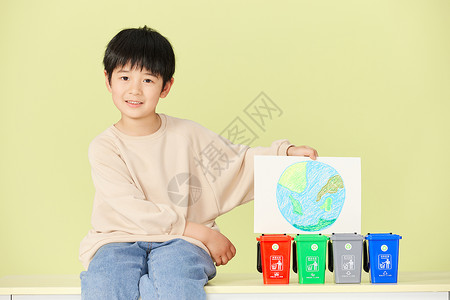 小男孩坐在垃圾分类桶旁图片