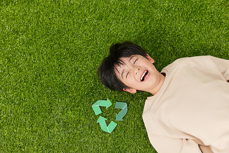 躺在草坪上的小男孩旁边放着可回收符号图片