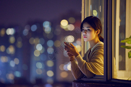 深夜阳台玩手机的年轻女性背景图片