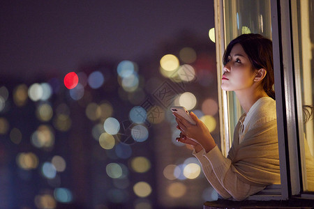 深夜阳台玩手机的年轻女性背景图片
