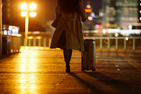 精英学生夜晚都市女性手提行李箱走在路上背景