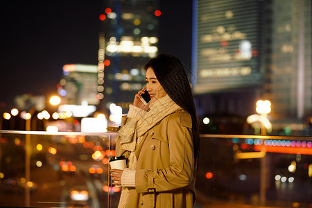 繁华阳台都市女性夜晚手握咖啡杯打电话背景