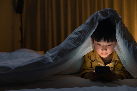 熬夜看书小男孩躲在被子下玩手机背景