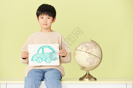 环保绘画坐在桌上的小男孩拿着手绘的汽车图片背景