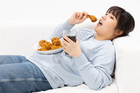 吃鸡腿女孩躺在沙发上的肥胖女性和美食背景