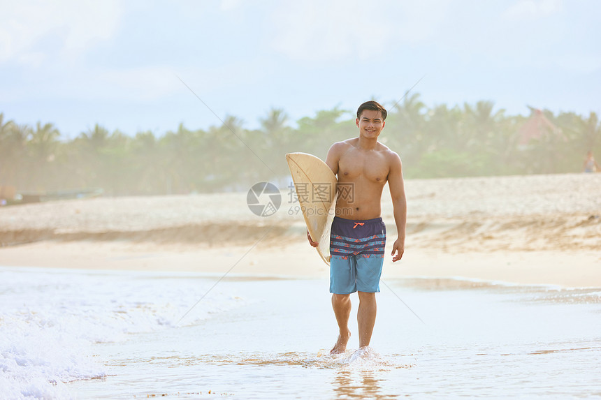 男青年手拿冲浪板海边行走图片
