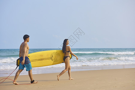 冲浪运动员年轻男女手拿冲浪板海边行走背景