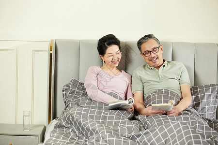 中老年夫妇坐在床上享受阅读的乐趣背景图片