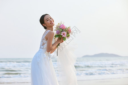 海边穿婚纱的美女手拿手捧花图片