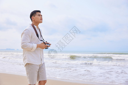 年轻男士拿着相机海边旅行拍照图片