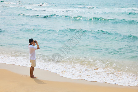 年轻男士拿着相机海边旅行拍照背影图片