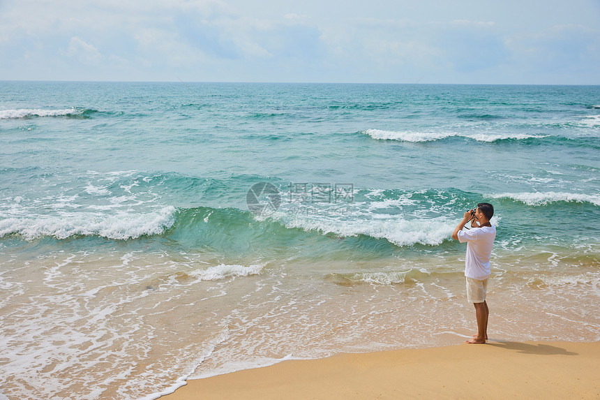 年轻男士拿着相机海边旅行拍照图片