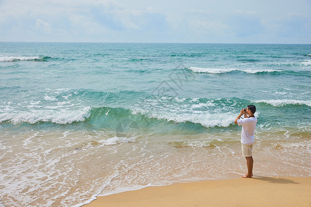 年轻男士拿着相机海边旅行拍照图片