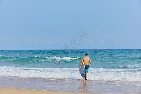 沙滩裤年轻男士拿着冲浪板海边行走背景
