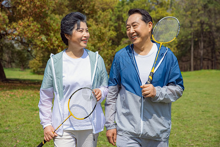 运动白天老年夫妇在公园打羽毛球背景