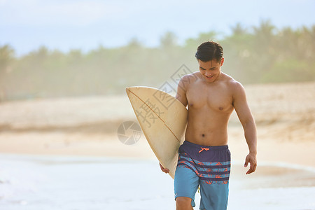 年轻男士拿着冲浪板海边行走背景图片
