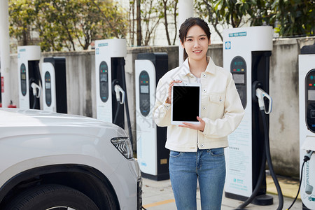 女性站在新能源汽车充电桩旁展示平板电脑图片