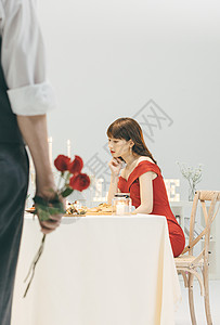 餐桌上等待的女生和手拿玫瑰的男生图片